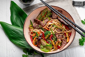 udon stir fry noodles with beef meat and vegetables in a plate on white wooden background.