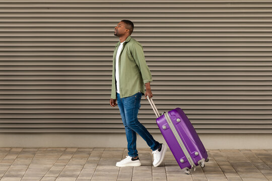 Wall Mural - Smiling African American Male Traveler Walking With Travel Suitcase Outdoors