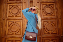 Happy Smiling Fashionable Woman Wearing Trendy Outfit With Blue Coat, Round Sunglasses, Classic Burgundy Color Leather Shoulder Bag. Copy, Empty Space For Text