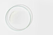 Petri dish on a light background. With a smear of white cream. Cosmetic cream, face mask, cream texture. View from above