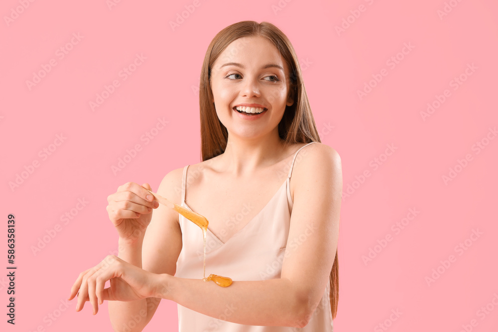 Young woman applying sugaring paste onto her arm against pink background