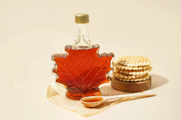 Wall Mural - Waffles, bottle and spoon of tasty maple syrup on beige background