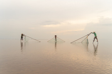 Silhouette of Vietnamese fisherman holding a net for catching freshwater fish in nature lake or river with reflection in morning time in Asia in Vietnam. People.