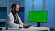 © DC Studio - General practitioner typing medical expertise on computer with greenscreen chroma key template working over hours in hospital office. Doctor checking patient report while planning healthcare treatment