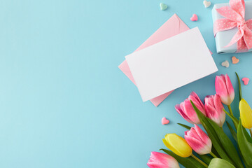 Wall Mural - Top view composition of giftbox with bow envelope letter hearts baubles bouquet of pink tulips on isolated pastel blue background with empty space. Happy Mother's Day concept