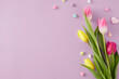 Mother's Day celebration idea. Top view composition of bouquet of pink yellow tulips and colorful hearts baubles on isolated lilac background with empty space