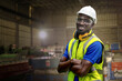 Portrait of manual African man worker is standing with confident with working suite dress and safety helmet in front machine for heavy industry factory. Steel metal sheet plant for production.
