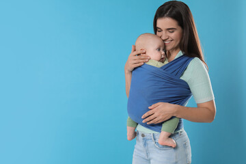 Canvas Print - Mother holding her child in sling (baby carrier) on light blue background. Space for text