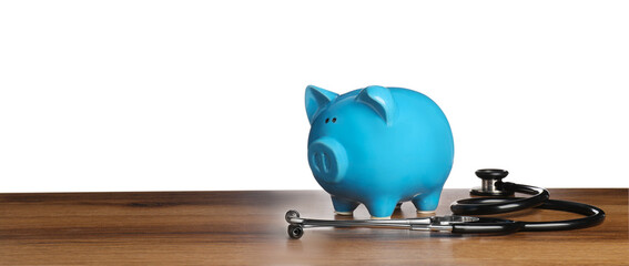 Piggy bank and stethoscope on wooden table against white background, space for text. Medical insurance