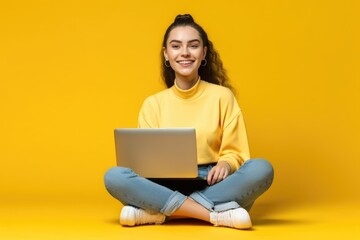 Wall Mural - Smiling attractive young woman sitting on the floor with her legs crossed holding a laptop computer