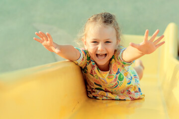 Child playing on outdoor wooden playground. Kids play on school or kindergarten yard. Active kid on colorful slide. Healthy summer activity for children