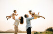 © sorapop - A cheerful Asian family enjoys a day out in nature, as the father and mother throw their toddler up into the sunny sky. The happy child enjoys the playful freedom of flying, captured in a photograph