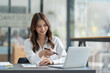 © crizzystudio - Asian businesswoman using a laptop to communicate Discuss and detail information about jobs online. Finance, accounting, income, and smiling happily at work.
