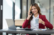 © crizzystudio - Asian businesswoman holding coffee mug relaxed and using phone browsing online applications and chatting after working on finance business and marketing at modern office.