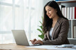© crizzystudio - Asian businesswoman, self-employed working on laptop computer typing e-commerce marketing financial report on real estate project in office management concept.
