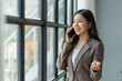 © crizzystudio - Asian business woman financially successful entrepreneur professional company executive Wearing a suit standing and talking on a mobile phone in business information in the office.