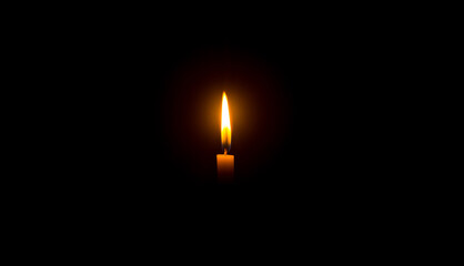 A single burning candle flame or light glowing on an orange candle on black or dark background on table in church for Christmas, funeral or memorial service with copy space