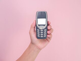 Fototapeta Uliczki - Close up hand holding mobile phone Nokia 3310 isolated on pink background. Female hand holding old used phone Nokia 3310.