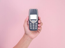 Close Up Hand Holding Mobile Phone Nokia 3310 Isolated On Pink Background. Female Hand Holding Old Used Phone Nokia 3310.