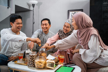 Wall Mural - Muslim friends chatting while taking snacks from a jar during a visit to celebrate Eid at a friend's house