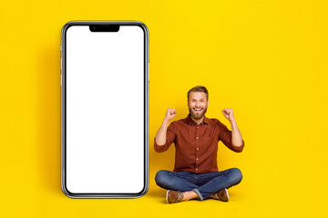 Sticker - Full size photo of delighted excited person sit floor raise fists achieve huge empty space telephone display isolated on yellow color background