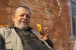 Outdoor portrait of smiling Ukrainian senior man against while standing against  brick wal and holding handmade patty filled with fried cabbage