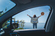 Happy cheerful young woman traveling on the sea by car. Standing overlooking the sea with hands up