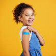 © Nina/peopleimages.com - Happy, portrait and child with a plaster in a studio for a wound, sore or injury on her arm. Happiness, smile and healthy girl kid model posing with a bandaid after a vaccination by yellow background