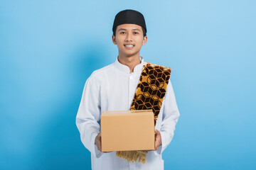 Wall Mural - Asian muslim man giving donations box or ramadan parcel isolated on blue background