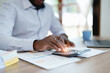 © Jirapong - middle age man American African using calculator for calculating and laptop computer with planning working on financial document, tax, exchange, accounting and Financial advisor