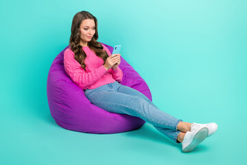 Sticker - Full length photo of lovely girl sitting bean bag use iphone write instagram facebook post empty space isolated on cyan color background