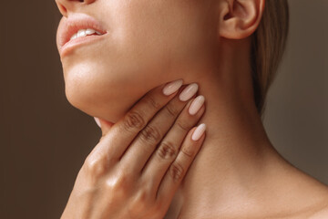 Cropped shot of young blonde woman with throat ache touching enlarged lymph nodes under jaw on her neck on dark background. Flu, cold, covid, tonsillitis, sars virus, inflamed tonsils. Sore throat