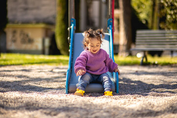 sweet caucasian little toddler girl with two tails having fun smiling widely sliding down the yellow