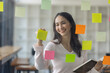 © David - Business female employee with many conflicting priorities arranging sticky notes commenting and brainstorming on work priorities colleague in a modern office.