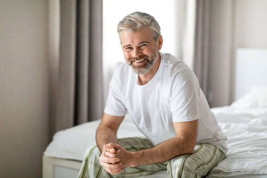 Wall Mural - Portrait of happy middle aged man sitting on bed, smiling