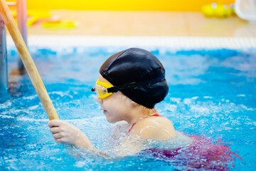 Child girl swimmer in red bathing suit on background of pool with glasses. Concept training sport swimming