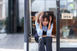 © amnaj - Female shopkeeper sitting stressed out at the store entrance frustrated by the economic impact.