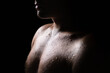 Sweat on skin. Wet sweaty body of a man. Exercise, gym fitness training and sport. Hard workout. Chest and shoulder light, black shadow. Shirtless guy in dark. Shower, sauna or rain. Water drops.