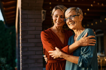 Wall Mural - Embraced senior woman and her daughter on patio at sunset.