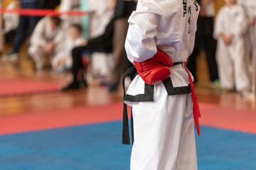 Taekwondo athlete with a black belt in a white kimono and red gloves at competitions.