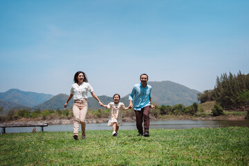 Wall Mural - Happy family in the nature travel. family on weekend playing together in the meadow with river Parents hold the child and daughter hands.health life insurance plan concept.