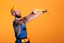 Confident Construction Worker Using Tape Measure To Take Measurements And Work On Refurbishment Project. Young Male Builder Holding Tapeline And Measuring For Renovation, Wearing Tools Belt.