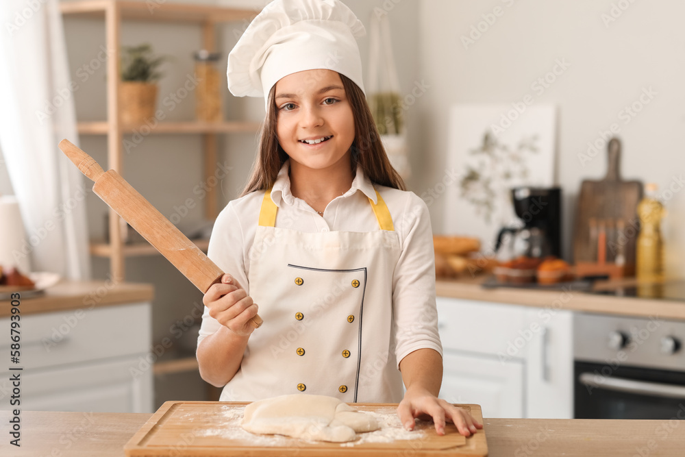 Little baker with rolling pin and dough at table in kitchen