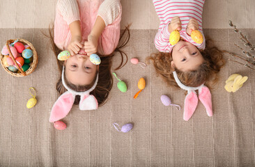 Wall Mural - Little girls in bunny ears with Easter eggs lying at home, top view