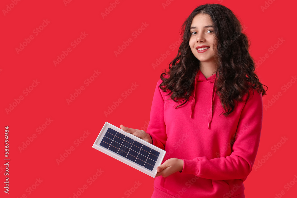 Teenage girl with portable solar panel on red background