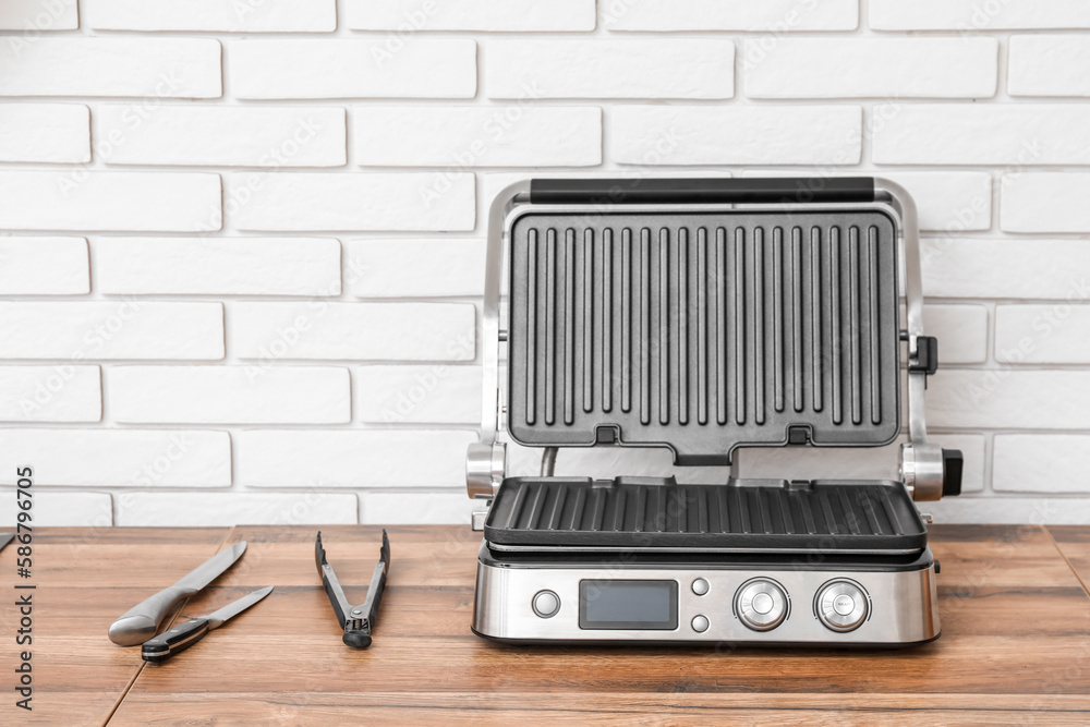 Modern electric grill on table near white brick wall