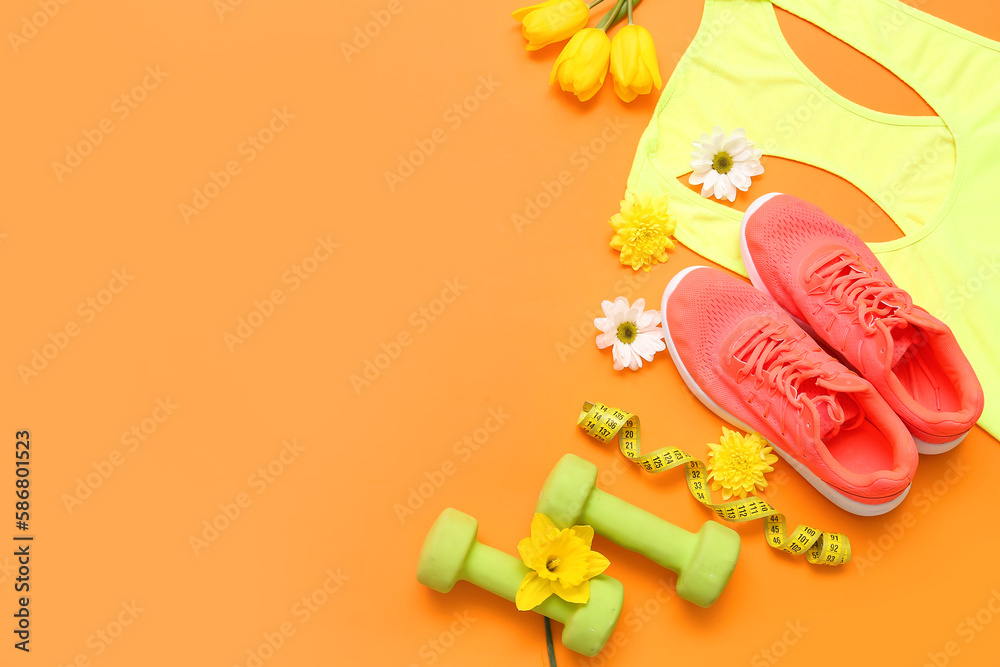 Sportswear with dumbbells and spring flowers on color background
