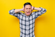 © Bangun Stock Photo - Handsome young Asian man frustrated wearing a plaid shirt covering his ears with his hands and keeping his eyes closed while screaming isolated on yellow background. people lifestyle concept