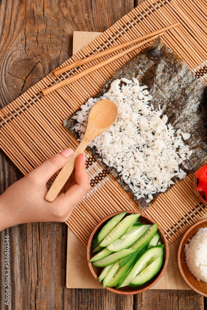 Woman preparing sushi rolls on wooden background