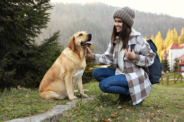 Canvas Print - Happy woman and adorable dog sitting on green grass in mountains. Traveling with pet